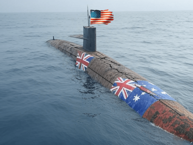 A battered submarine with Australian flags over the hull and the US flag flying from the fairwater.