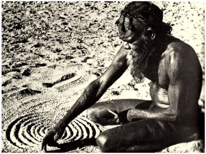 An Aboriginal man drawing concentric circles in sand.